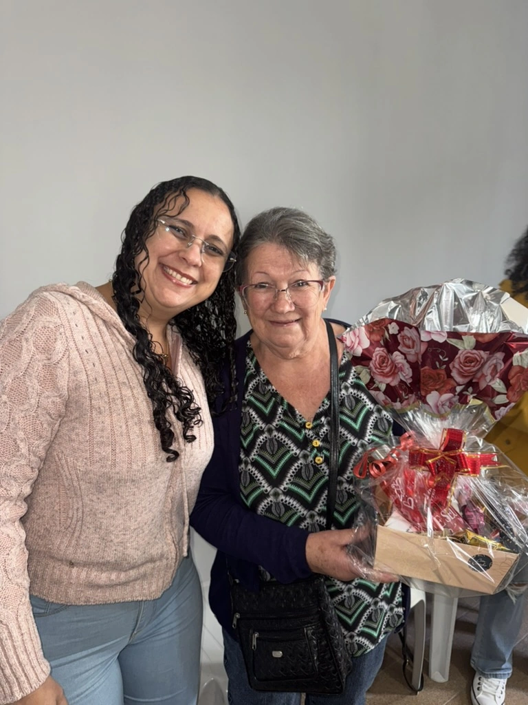 Duas mulheres posam juntas ao lado de um presente com flores.