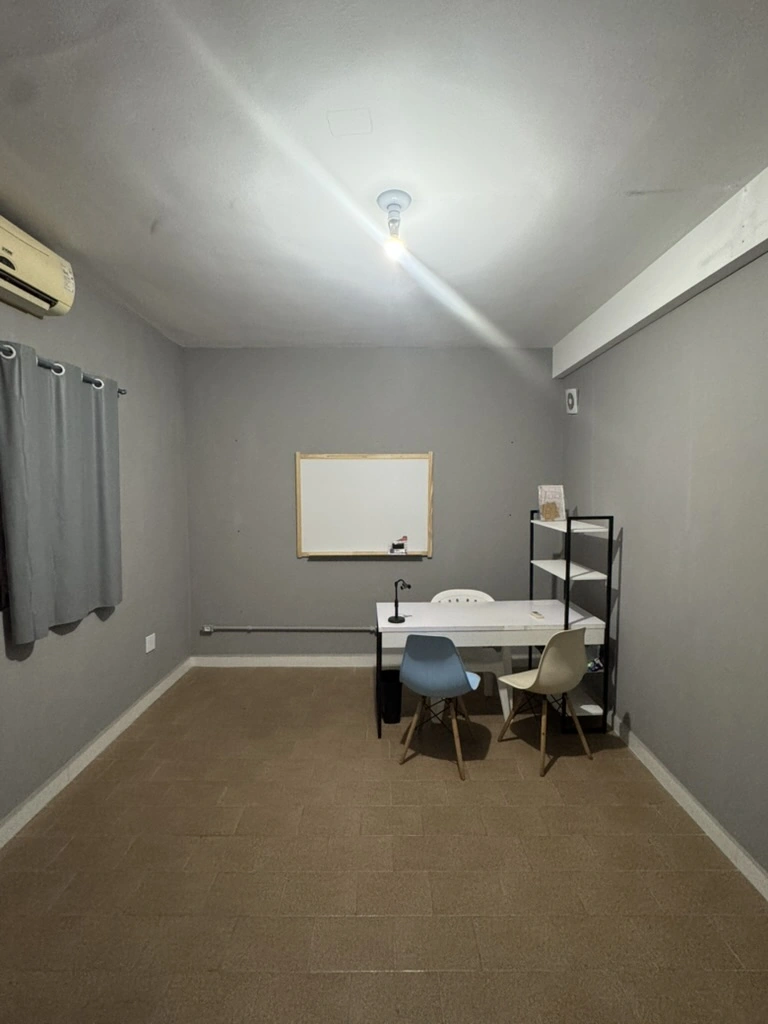 Sala 2 - Auditório com mesa branca, cadeiras coloridas, quadro e estante em um ambiente amplo.