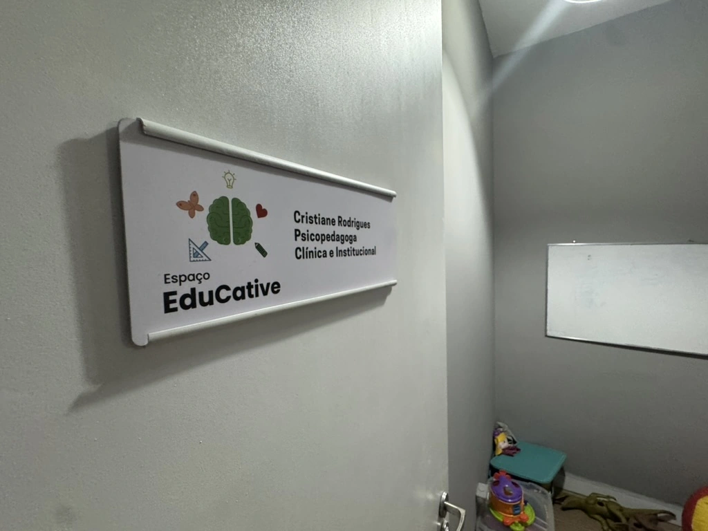 Placa do Espaço Educative na parede da sala de atendimento, ao lado de uma lousa branca.