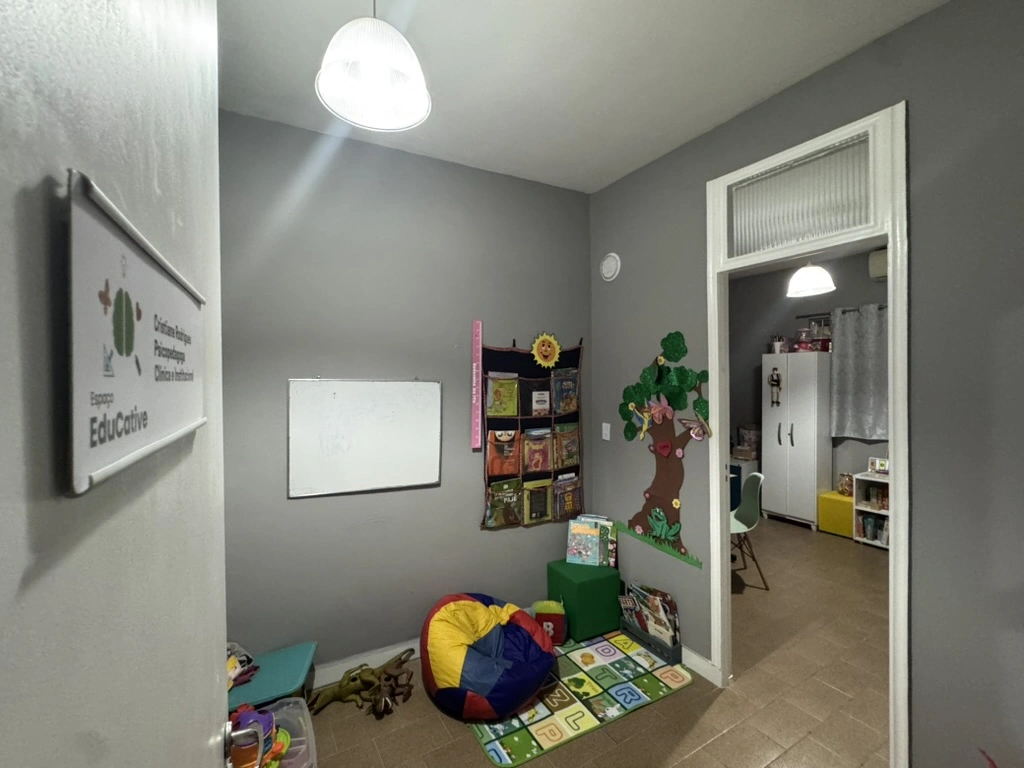 Cantinho infantil com estante de livros, árvore decorativa e tapete de atividades.