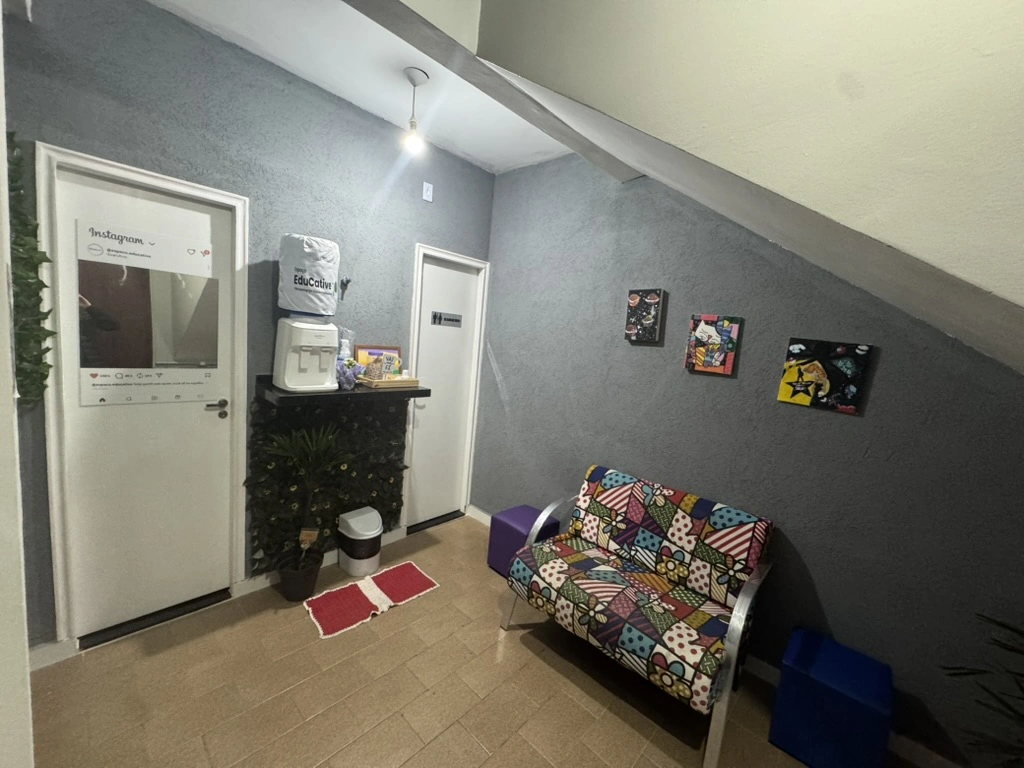 Sala de espera com sofá colorido, quadros decorativos e espaço de circulação.