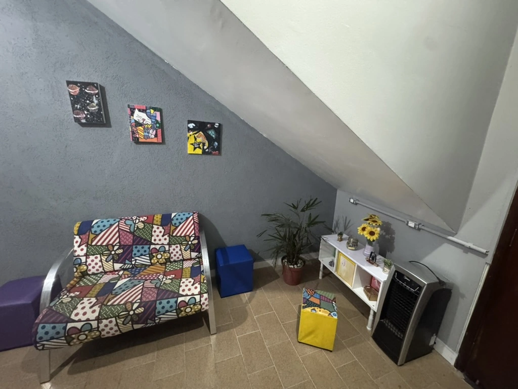 Sofá colorido, quadros infantis e um arranjo de girassóis na sala de espera.